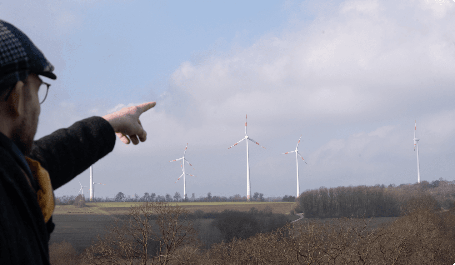 Ralf Marpert zeigt auf Windkraftanlagen in der Landschaft